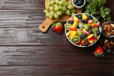 Photo of Tasty fruit salad in bowl and ingredients on wooden table, flat lay. Space for text