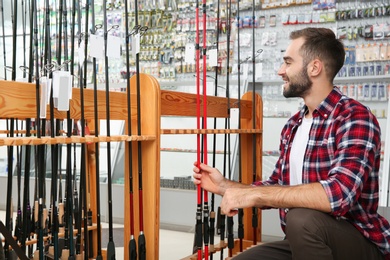 Man choosing fishing rod in sports shop. Space for text