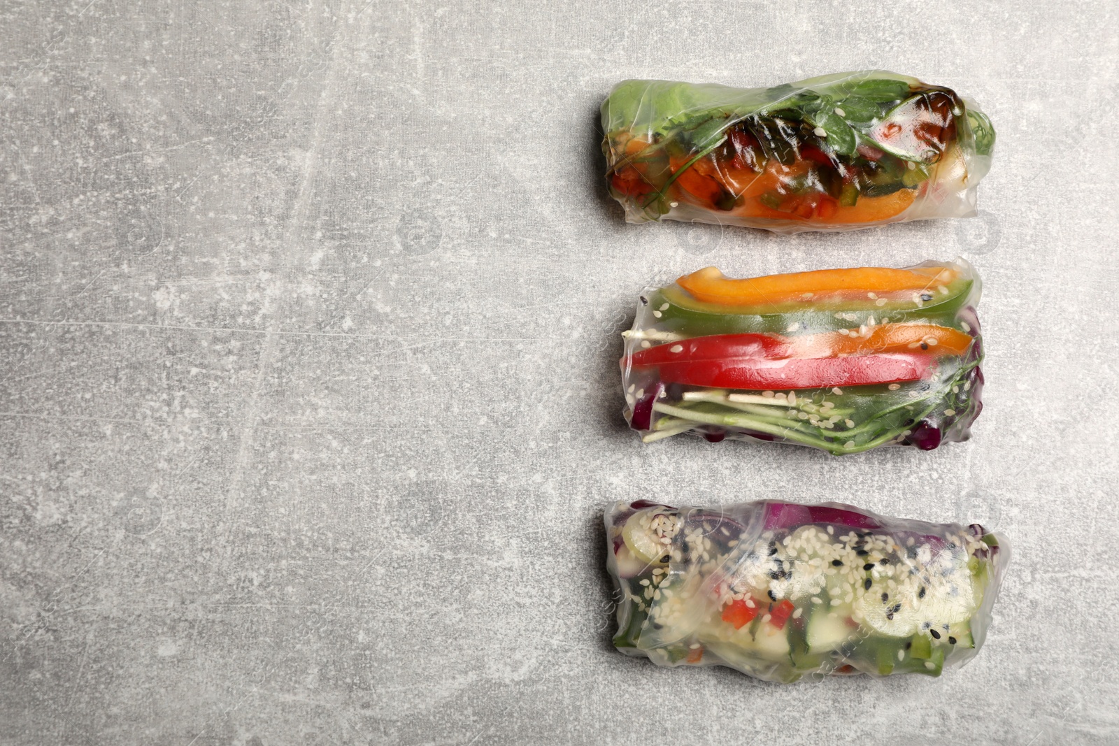 Photo of Different delicious rolls wrapped in rice paper on grey table, flat lay. Space for text