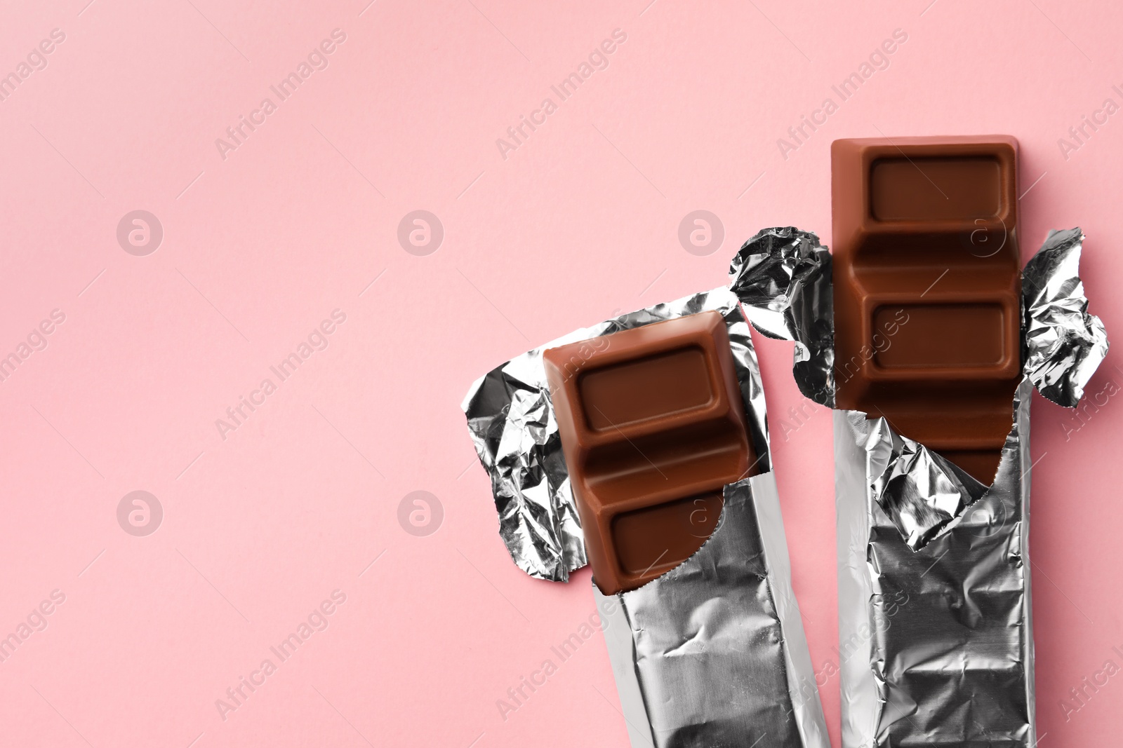 Photo of Delicious chocolate bars wrapped in foil on pink background, flat lay. Space for text