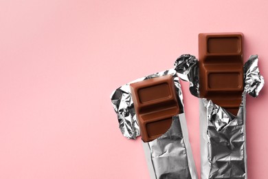 Delicious chocolate bars wrapped in foil on pink background, flat lay. Space for text