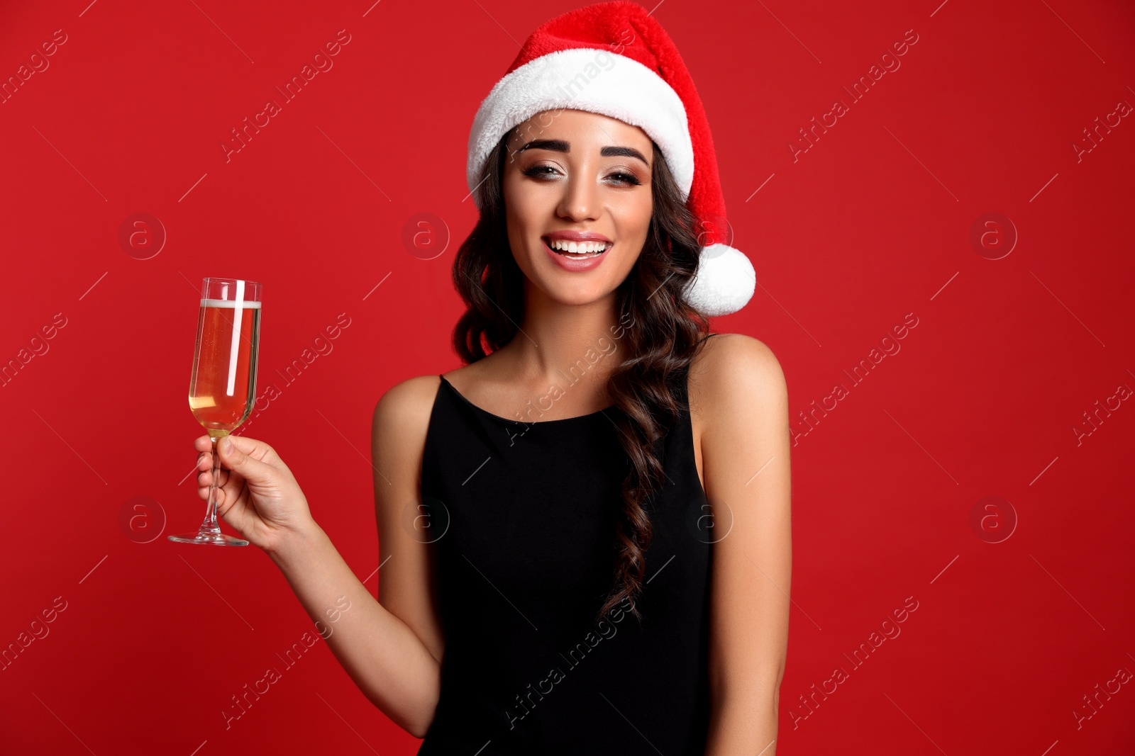 Photo of Beautiful woman in Santa hat holding glass of champagne on red background. Christmas party