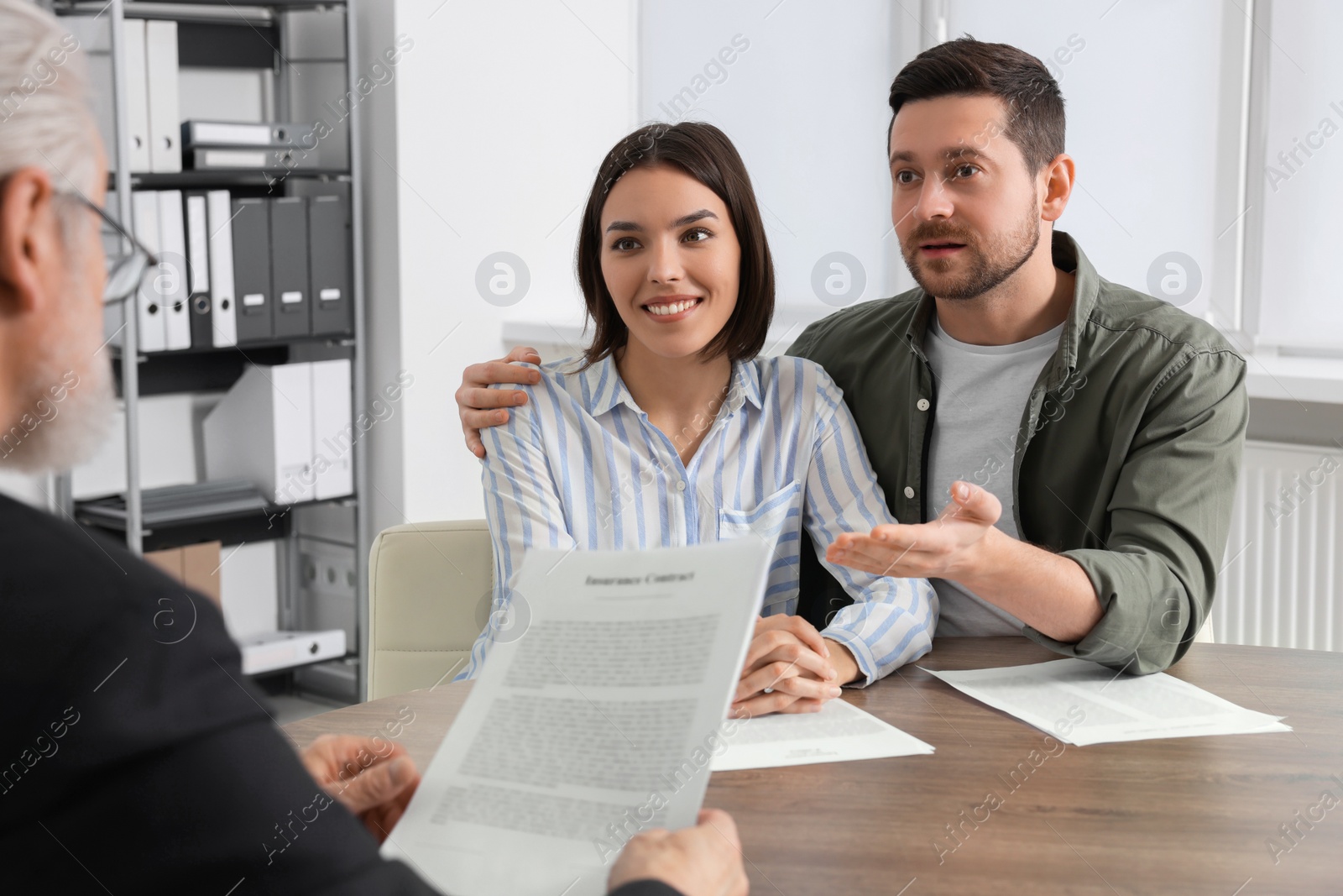 Photo of Young couple consulting insurance agent about pension plan at wooden table indoors