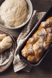 Photo of Fresh dough with flour and tasty braided bread on wooden table, flat lay. Traditional Shabbat challah