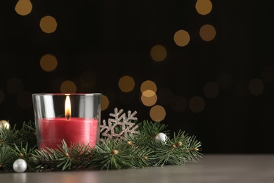 Burning candle with Christmas decor on table against blurred lights. Space for text