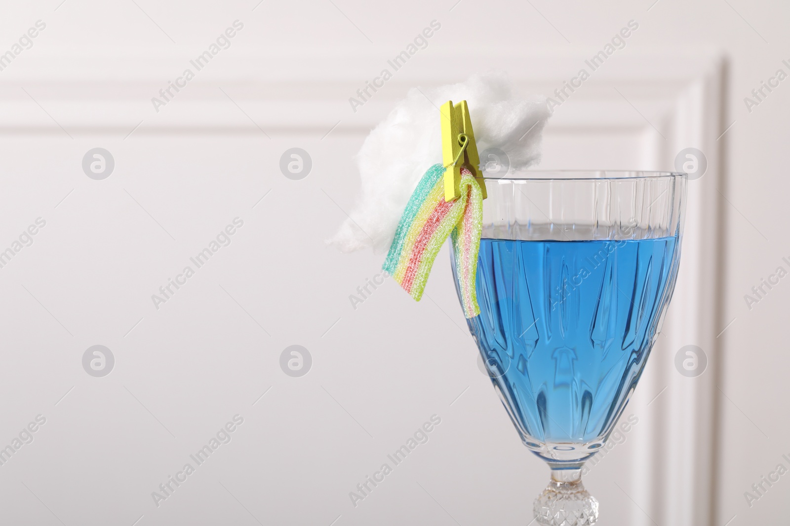 Photo of Bright cocktail in glass decorated with cotton candy and sour rainbow belt on white background, closeup. Space for text