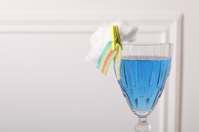 Photo of Bright cocktail in glass decorated with cotton candy and sour rainbow belt on white background, closeup. Space for text