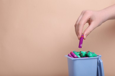 Photo of Woman putting used AAA size battery into recycling bin on beige background, closeup. Space for text