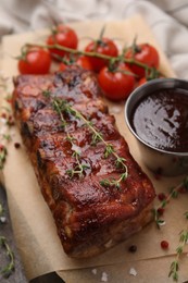 Photo of Tasty roasted pork ribs served with thyme, sauce and tomatoes on table, closeup