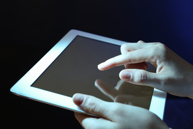 Photo of Woman using tablet on dark background, closeup