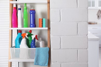 Rack with detergents and cleaning accessories near white wall indoors. Space for text