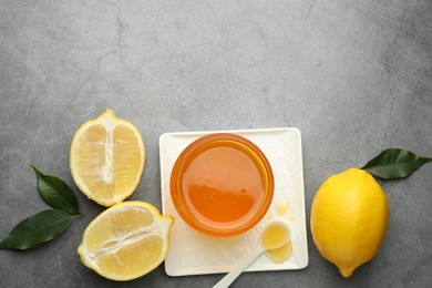 Photo of Sweet honey and fresh lemons on grey table, flat lay. Space for text