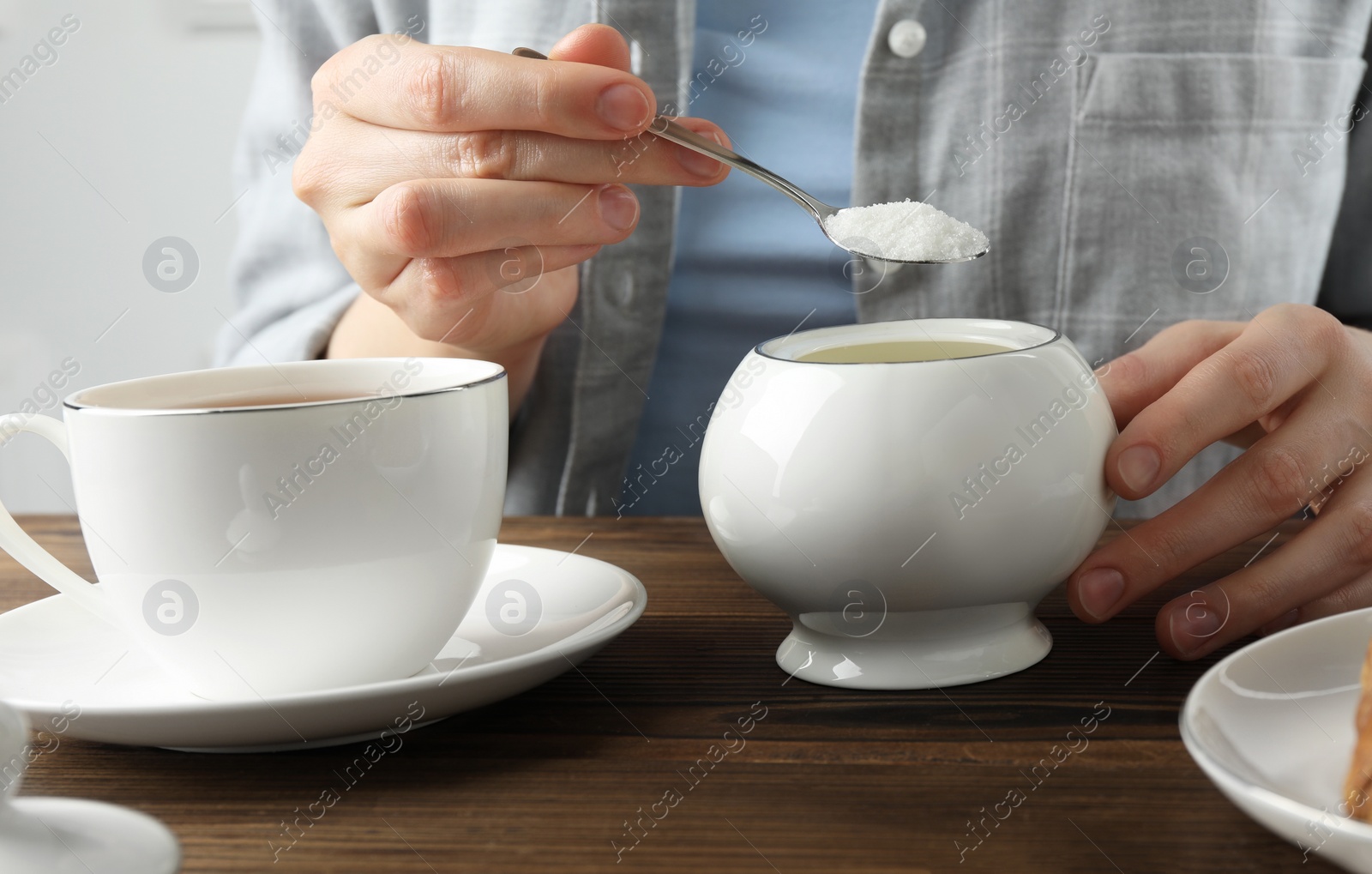 Photo of Woman adding sugar into cup of tea at wooden table, closeup