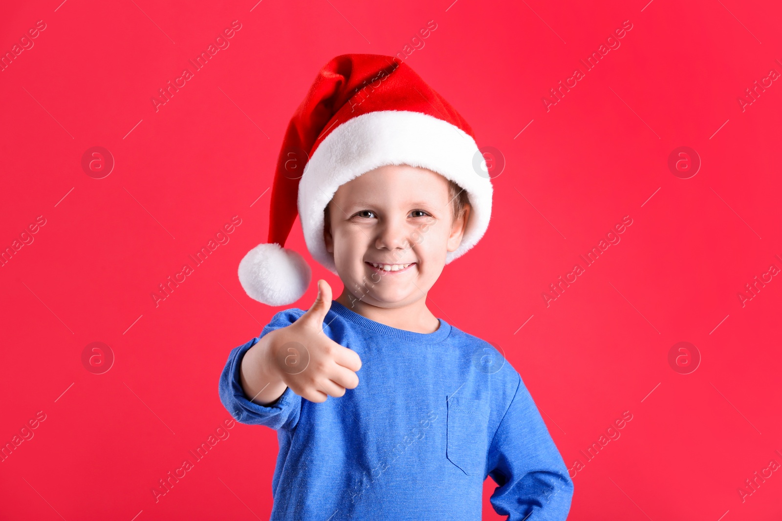Photo of Cute little boy wearing Santa Claus hat on red background