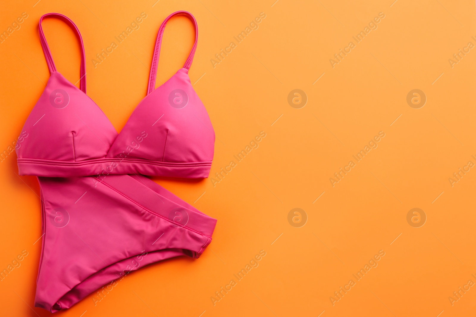 Photo of Beautiful pink bikini on orange background, top view. Space for text