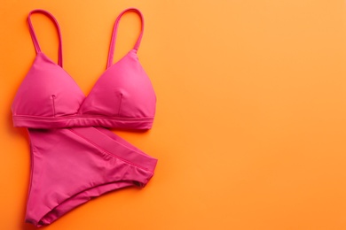 Photo of Beautiful pink bikini on orange background, top view. Space for text