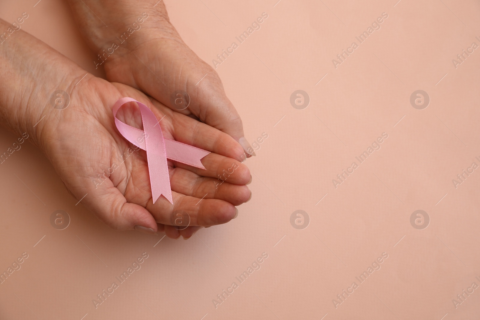 Photo of Senior woman holding pink ribbon on beige background, top view with space for text. Breast cancer awareness