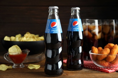 MYKOLAIV, UKRAINE - FEBRUARY 16, 2021: Glass bottles of Pepsi and snacks on wooden table