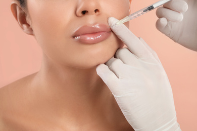 Photo of Young woman getting lips injection on peach background, closeup