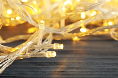 Glowing Christmas lights on wooden table, closeup