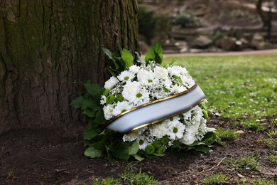 Photo of Funeral wreath of flowers with ribbon near tree outdoors