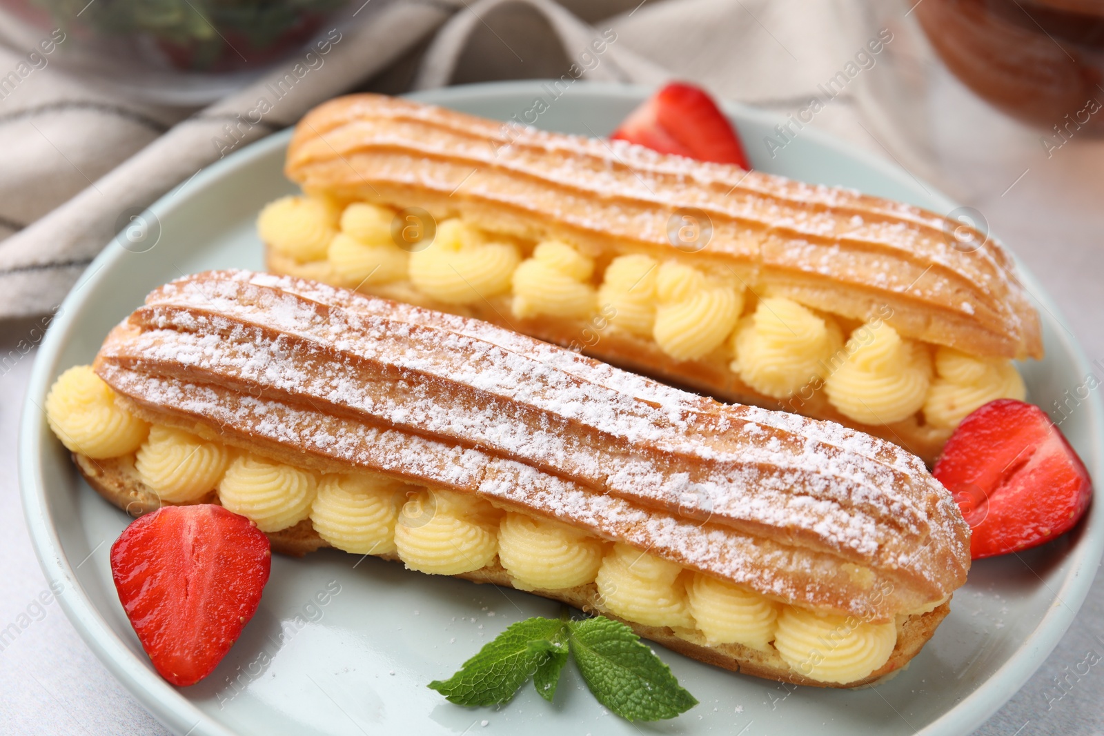 Photo of Delicious eclairs filled with cream, strawberries and mint on table, closeup