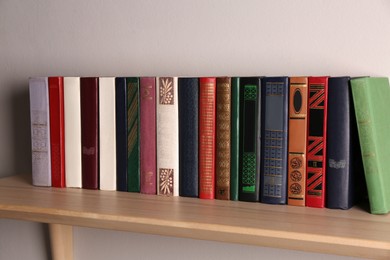 Wooden shelf with different books on light wall
