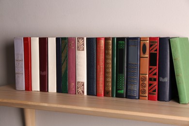 Photo of Wooden shelf with different books on light wall