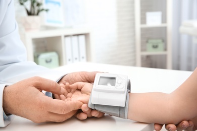 Doctor checking little girl's pulse with medical device in hospital, closeup