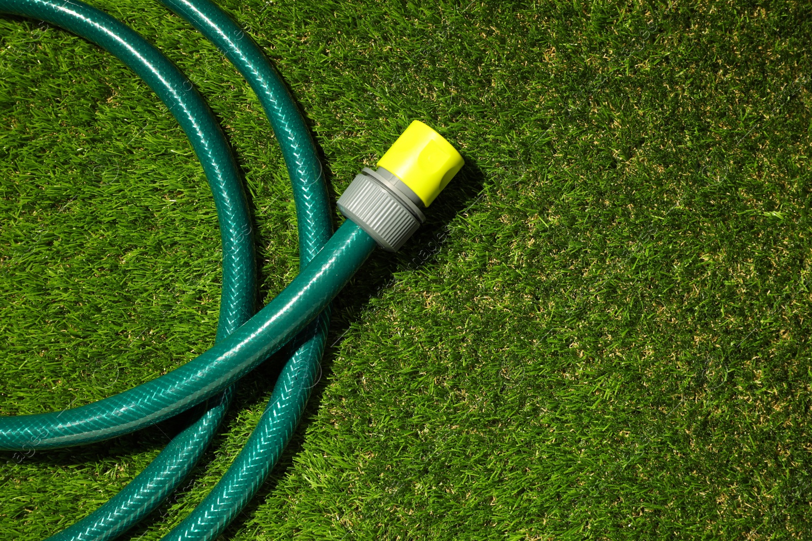 Photo of Watering hose on green grass, top view. Space for text
