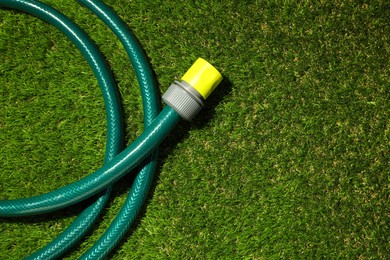 Photo of Watering hose on green grass, top view. Space for text