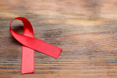 Photo of Closeup view of red ribbon on wooden background, space for text. AIDS disease awareness