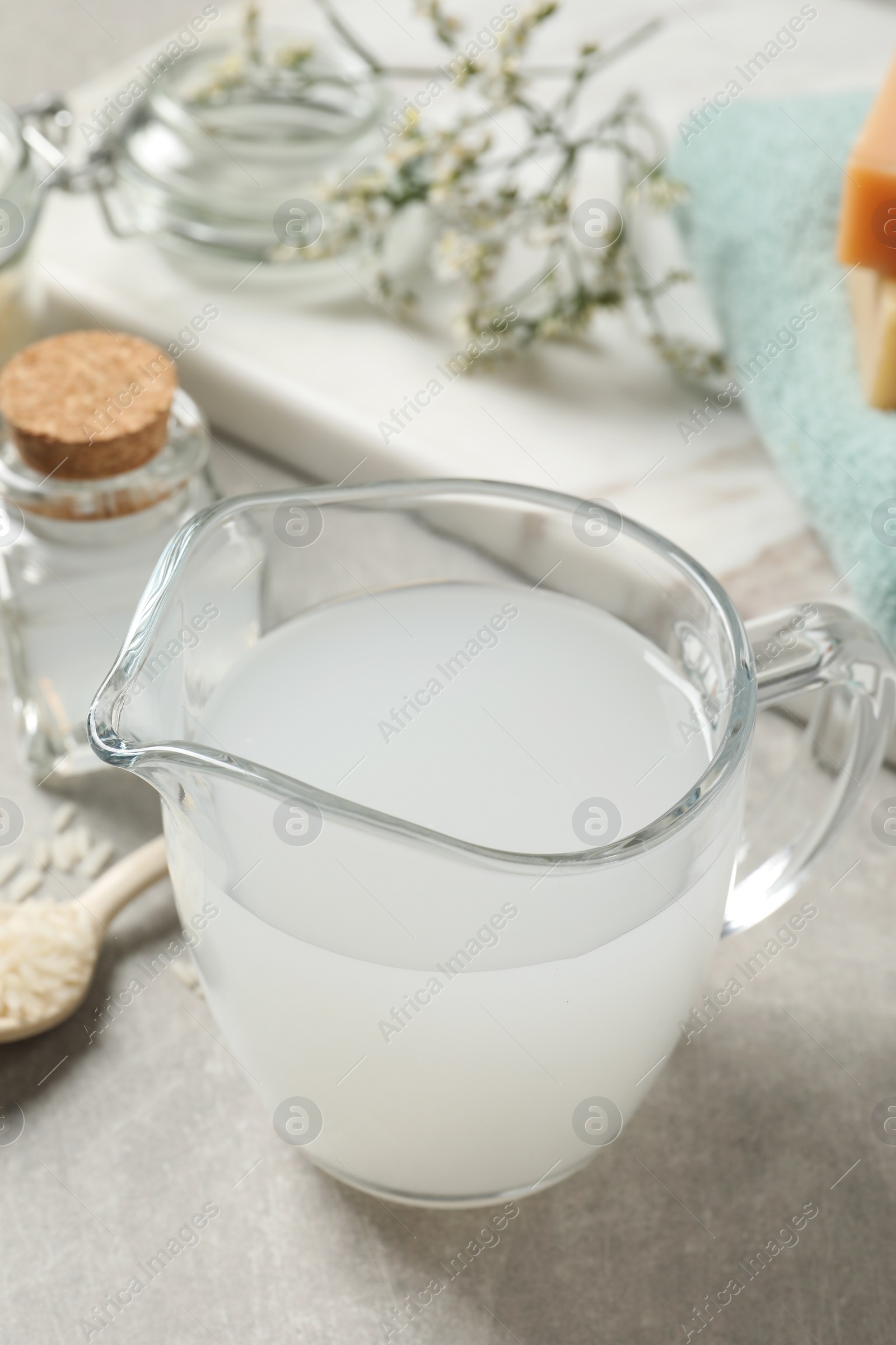 Photo of Glass jug with natural rice water on light grey table, closeup