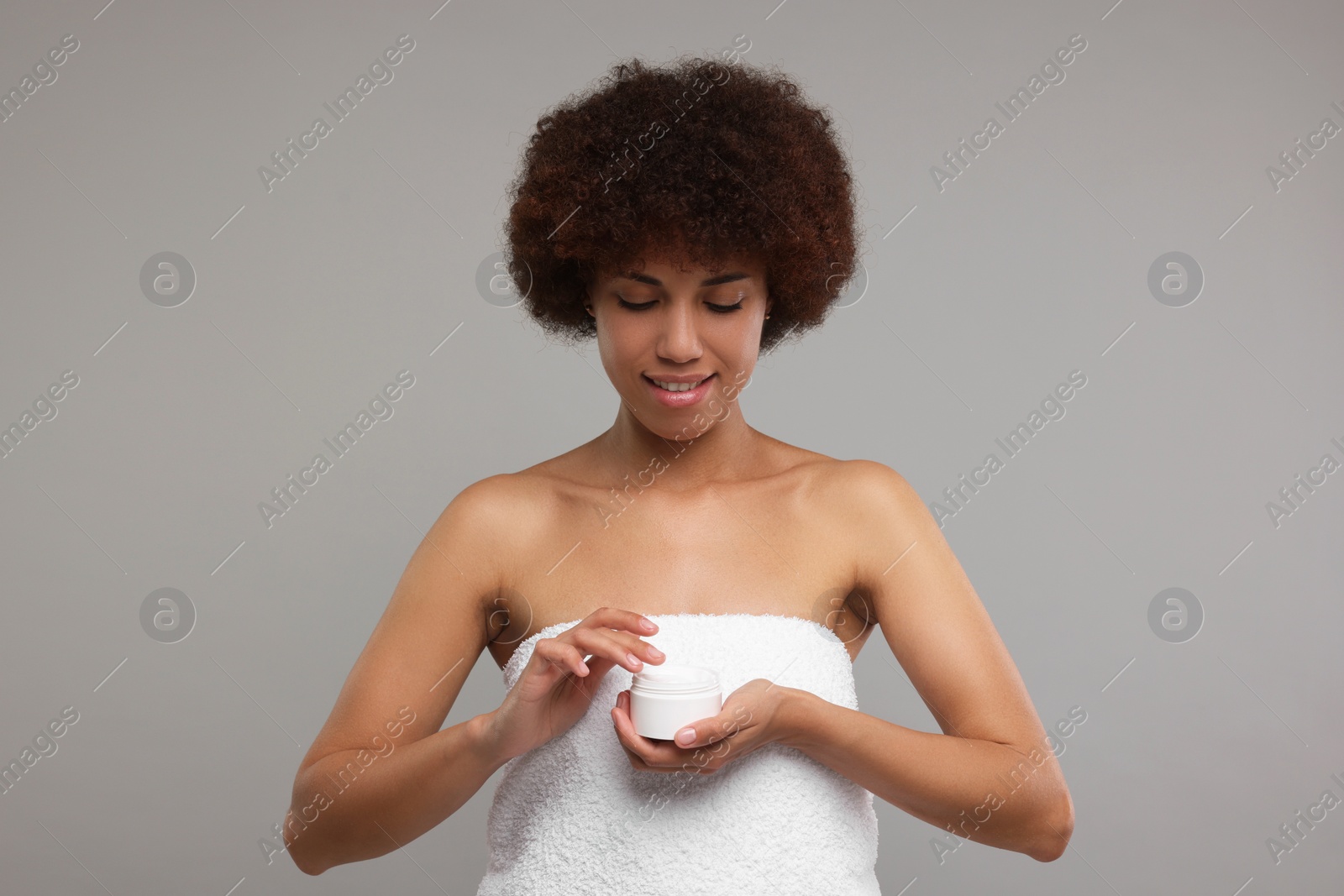 Photo of Beautiful young woman holding body cream on grey background