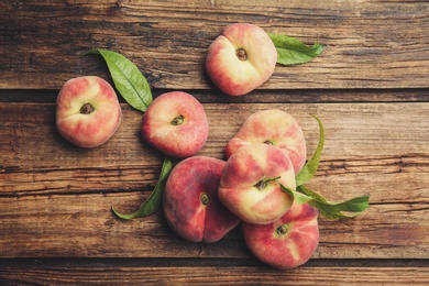 Fresh ripe donut peaches with leaves on wooden table, flat lay