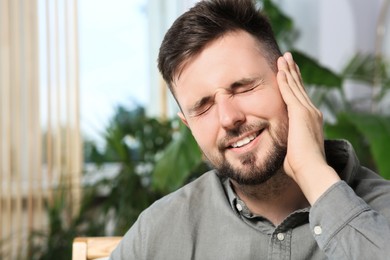 Photo of Young man suffering from ear pain at home. Space for text