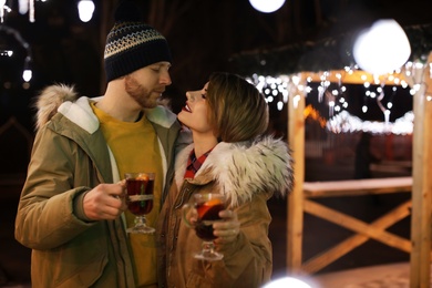 Photo of Young couple with cups of mulled wine at winter fair. Space for text