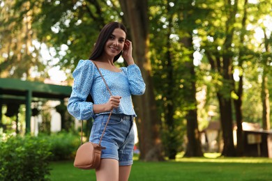 Photo of Beautiful young woman with stylish bag at park outdoors, space for text