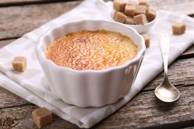 Delicious creme brulee in bowl, sugar cubes and spoon on wooden table, closeup