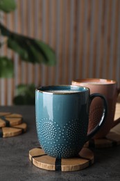 Mugs of hot drink with stylish cup coasters on grey table
