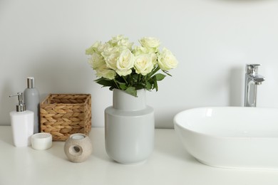 Photo of Vase with beautiful white roses and toiletries near sink in bathroom