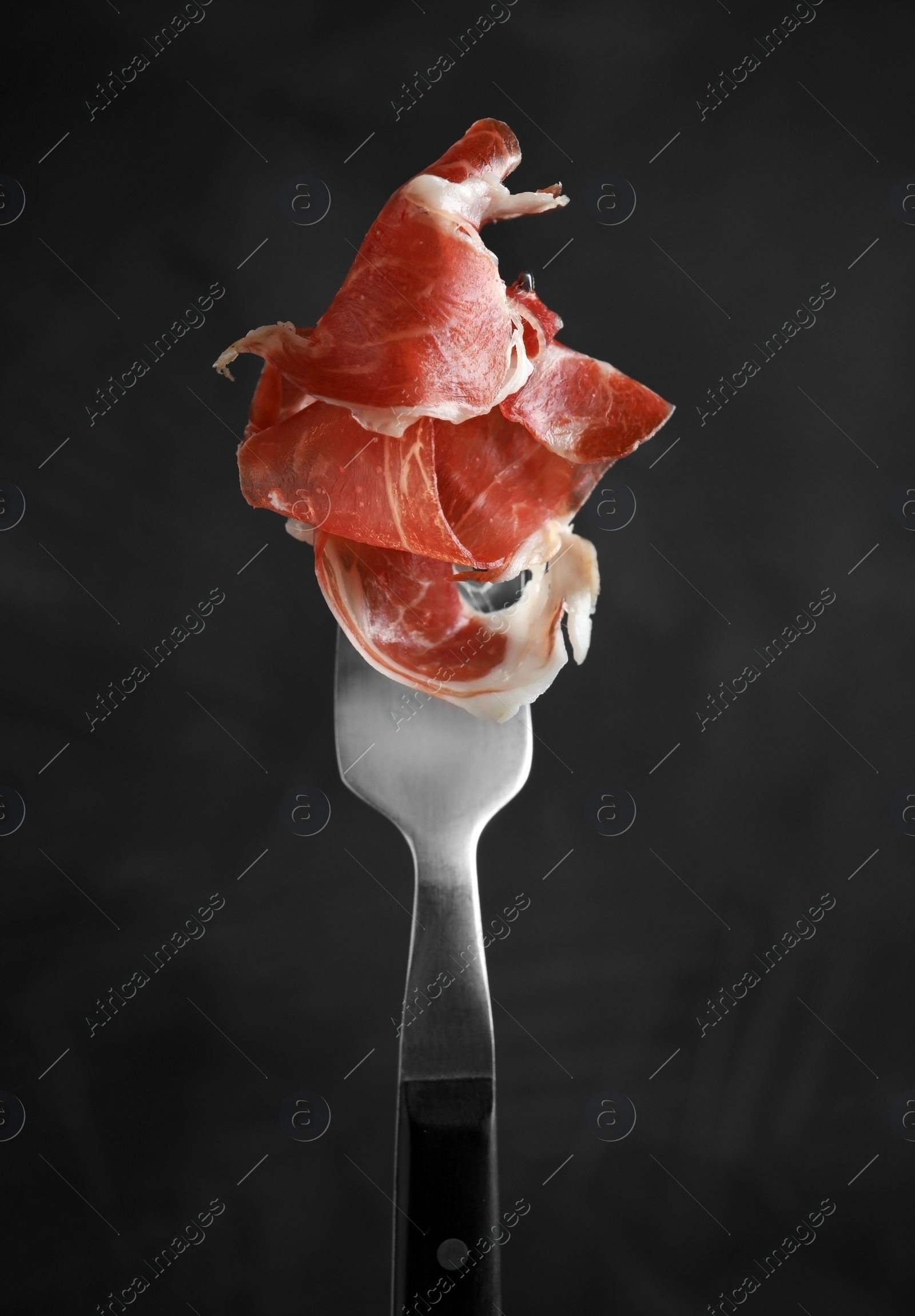 Photo of Tasty prosciutto on fork against dark grey background