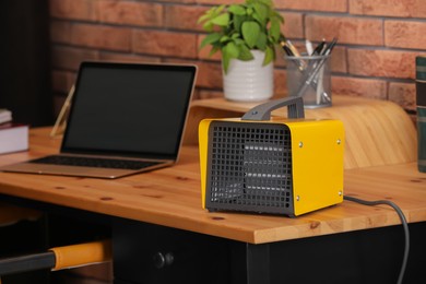 Modern electric heater near laptop on wooden table in office