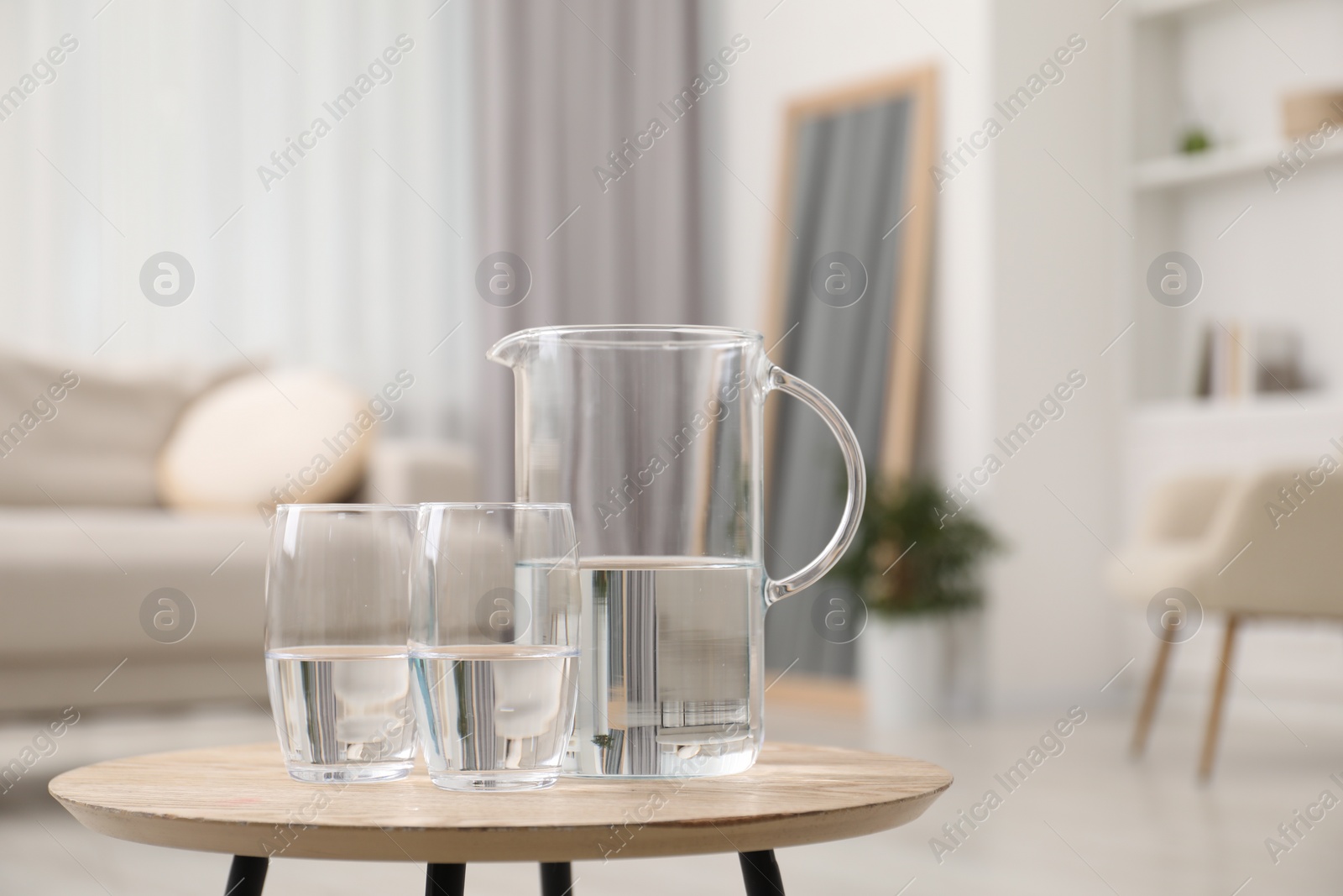 Photo of Jug and glasses with clear water on wooden table indoors. Space for text