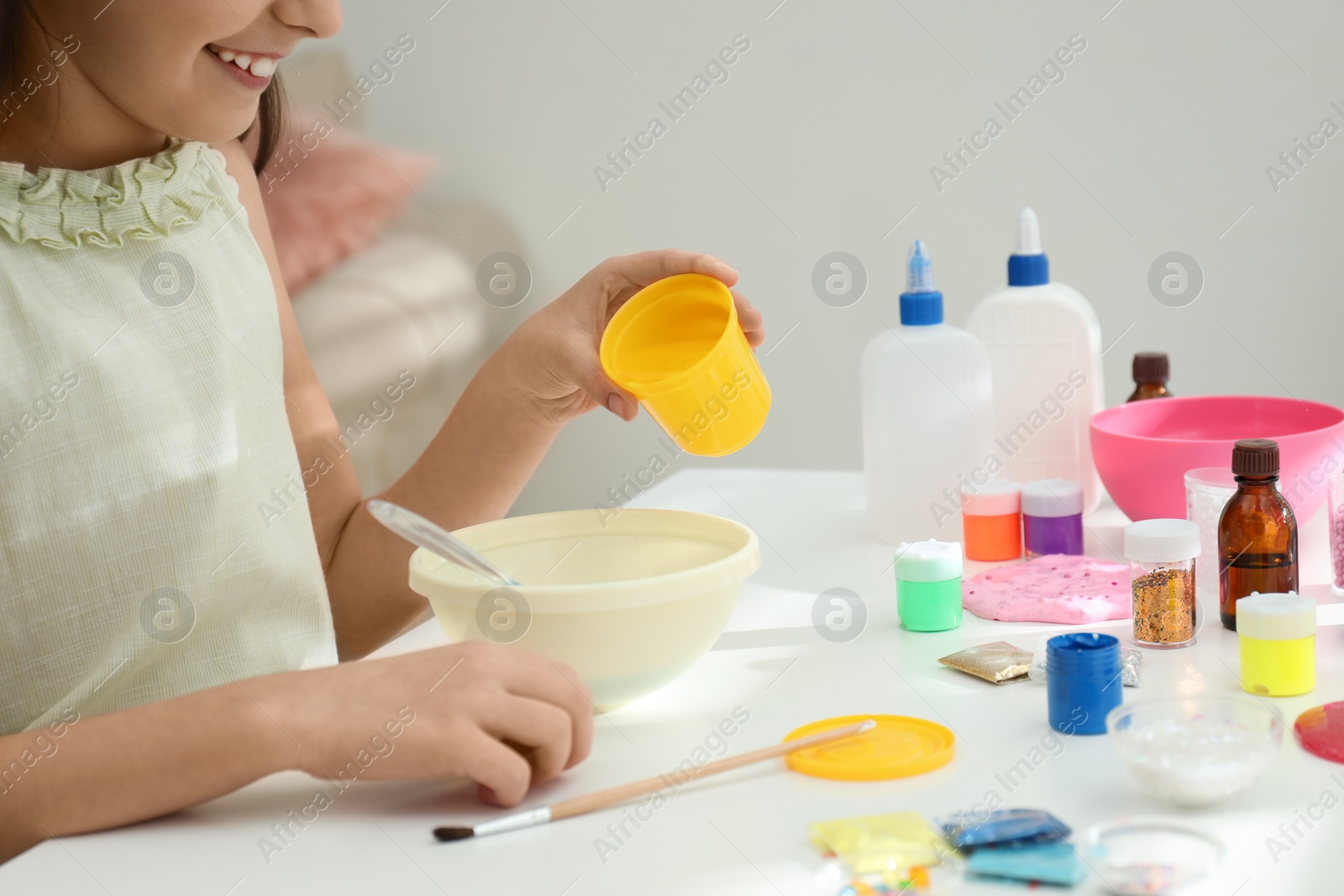 Photo of Little girl making homemade slime toy at table, closeup