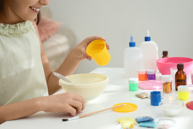 Photo of Little girl making homemade slime toy at table, closeup