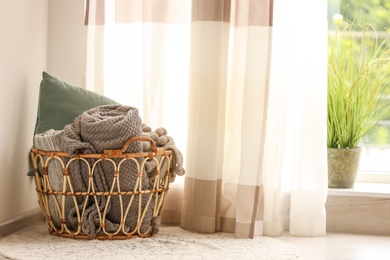 Wicker basket with rolled blankets and pillow indoors, space for text. Idea for interior design