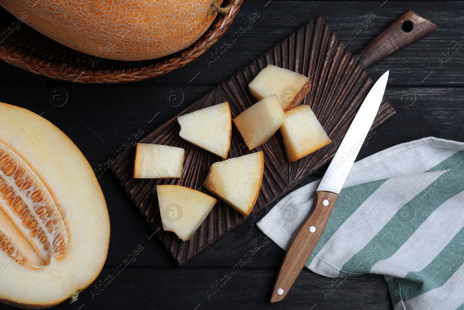 Photo of Pieces of delicious honey melon on black wooden table, flat lay