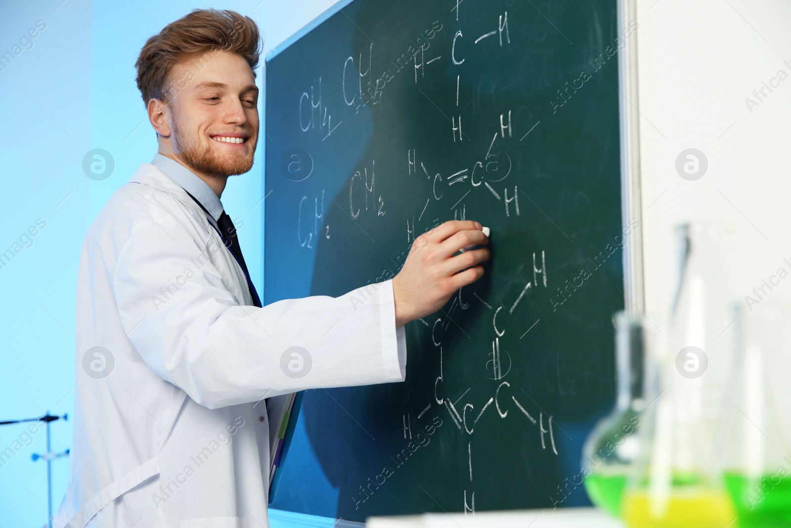 Photo of Male scientist writing chemical formula on chalkboard indoors