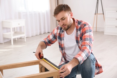 Photo of Young working man using measure tape at home, space for text